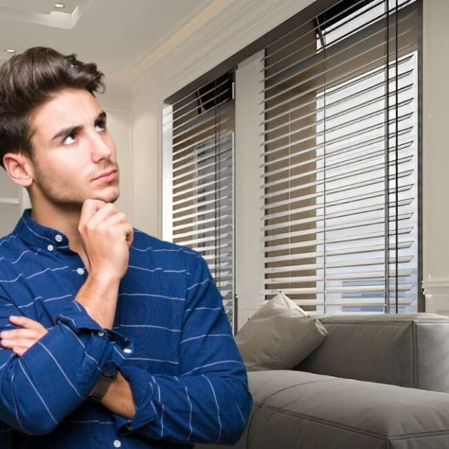 A man standing in a modern living room, looking thoughtful about the cost of blinds in Canada